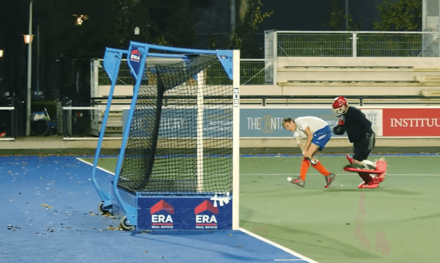 Fast-paced field hockey game with goalies, players, and a goalpost on an outdoor sports court, highlighting athletic performance and team sports.