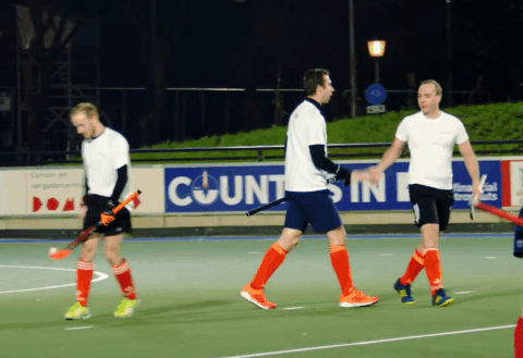 Energetic field hockey players celebrating on an outdoor synthetic turf pitch during night time, showcasing teamwork, sportsmanship, and athleticism.