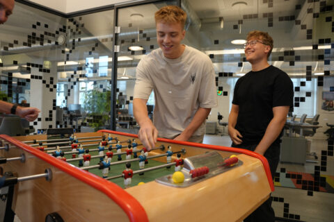 Playing foosball game at Keylane careers office with young professionals in modern workspace environment demonstrating a fun, collaborative workplace culture.