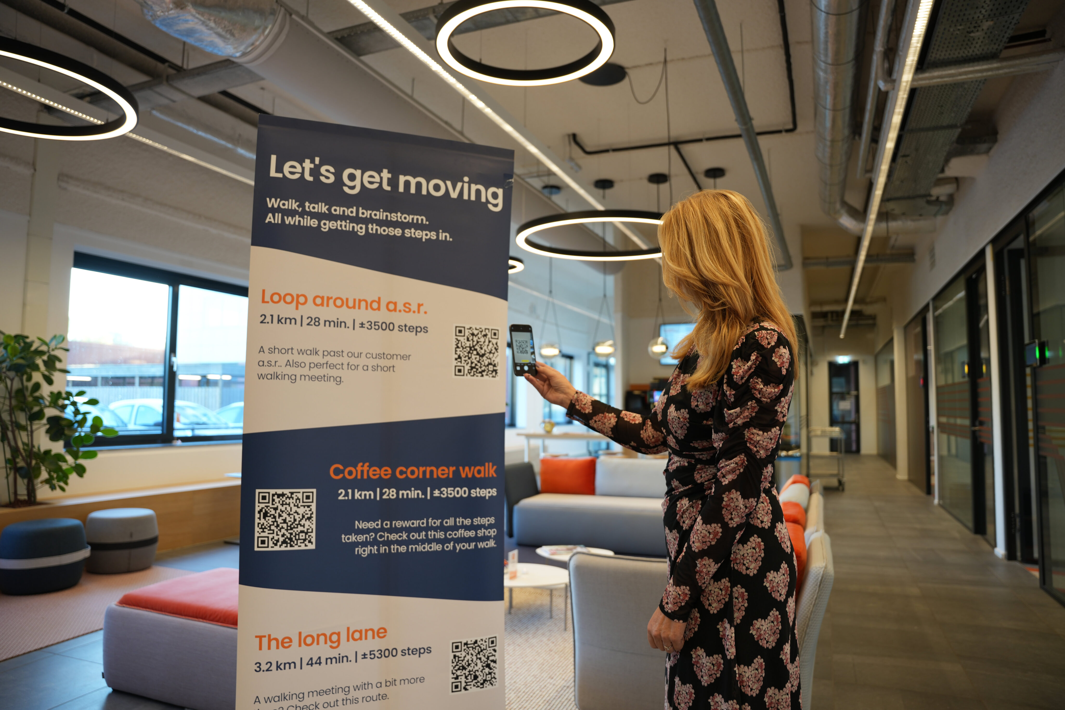 Enjoying a modern office space with a motivational "Let's get moving" signage promoting walking routes, emphasizing employee wellness and active breaks for a productive work environment.