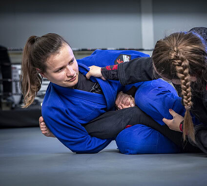 Female Brazilian Jiu-Jitsu practitioners training and competing in a gym, demonstrating submission techniques and grappling skills in a professional martial arts environment.