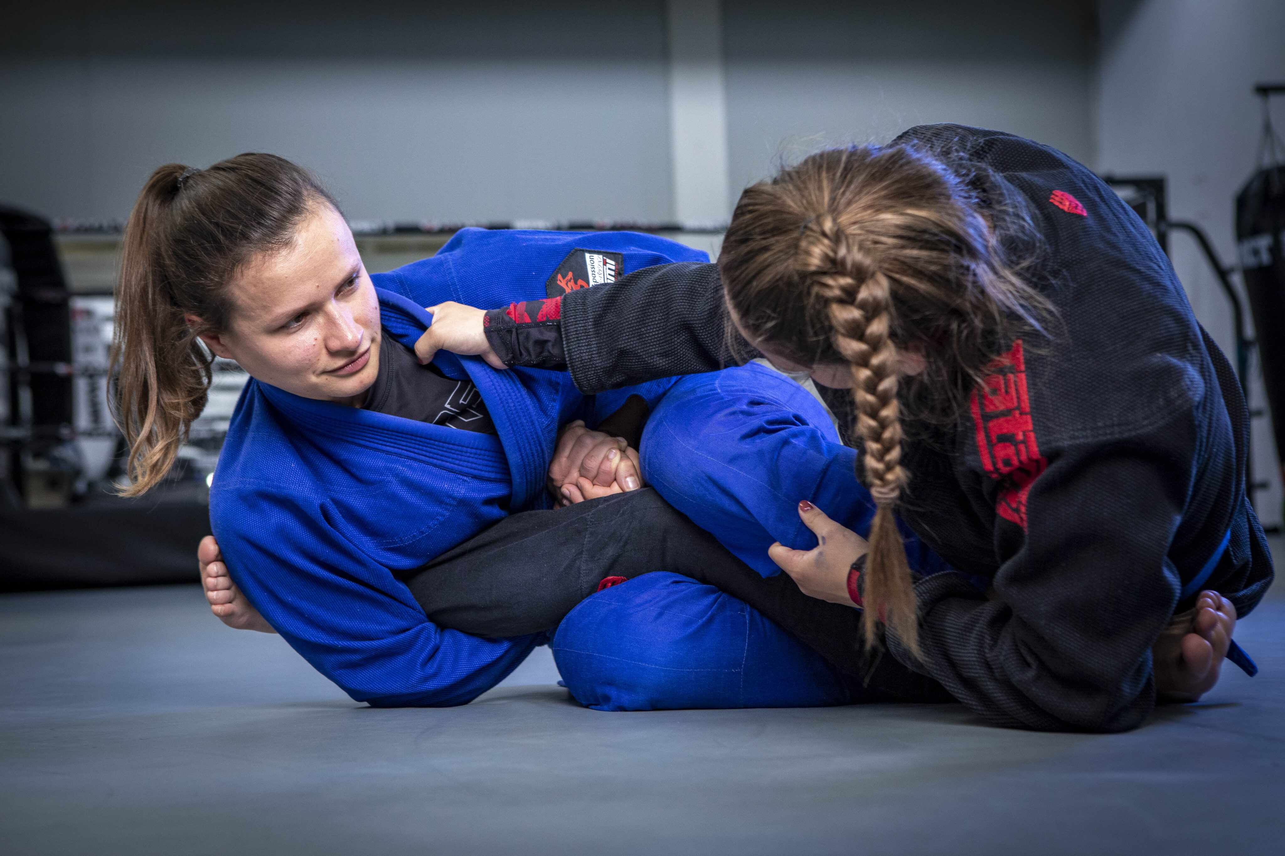Female Brazilian Jiu-Jitsu practitioners training and competing in a gym, demonstrating submission techniques and grappling skills in a professional martial arts environment.