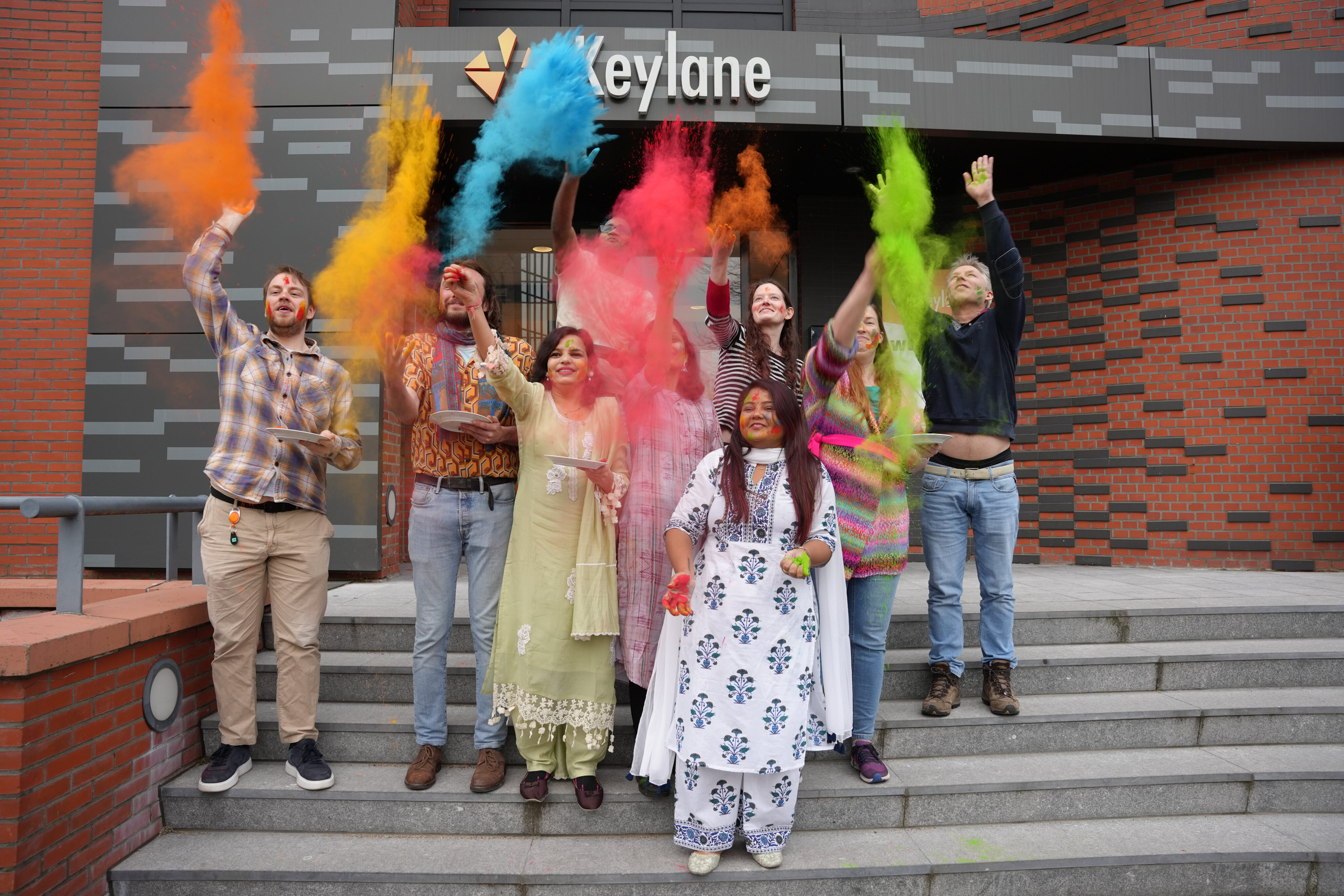 Colorful group celebrating Holi festival outside Keylane office, celebrating diversity, inclusion, and vibrant company culture at Keylane Careers.