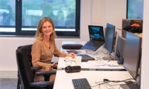 Flexible office workspace with a woman smiling at her desk, multiple computer screens, and a laptop, showcasing a modern work environment and career opportunities at Keylane.