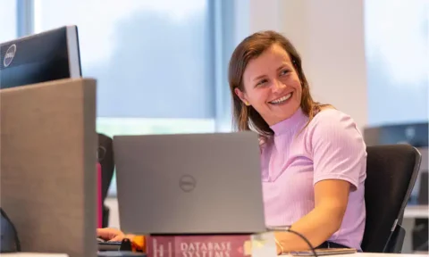 Coding and data analytics professional smiling at her desk in a modern office environment.