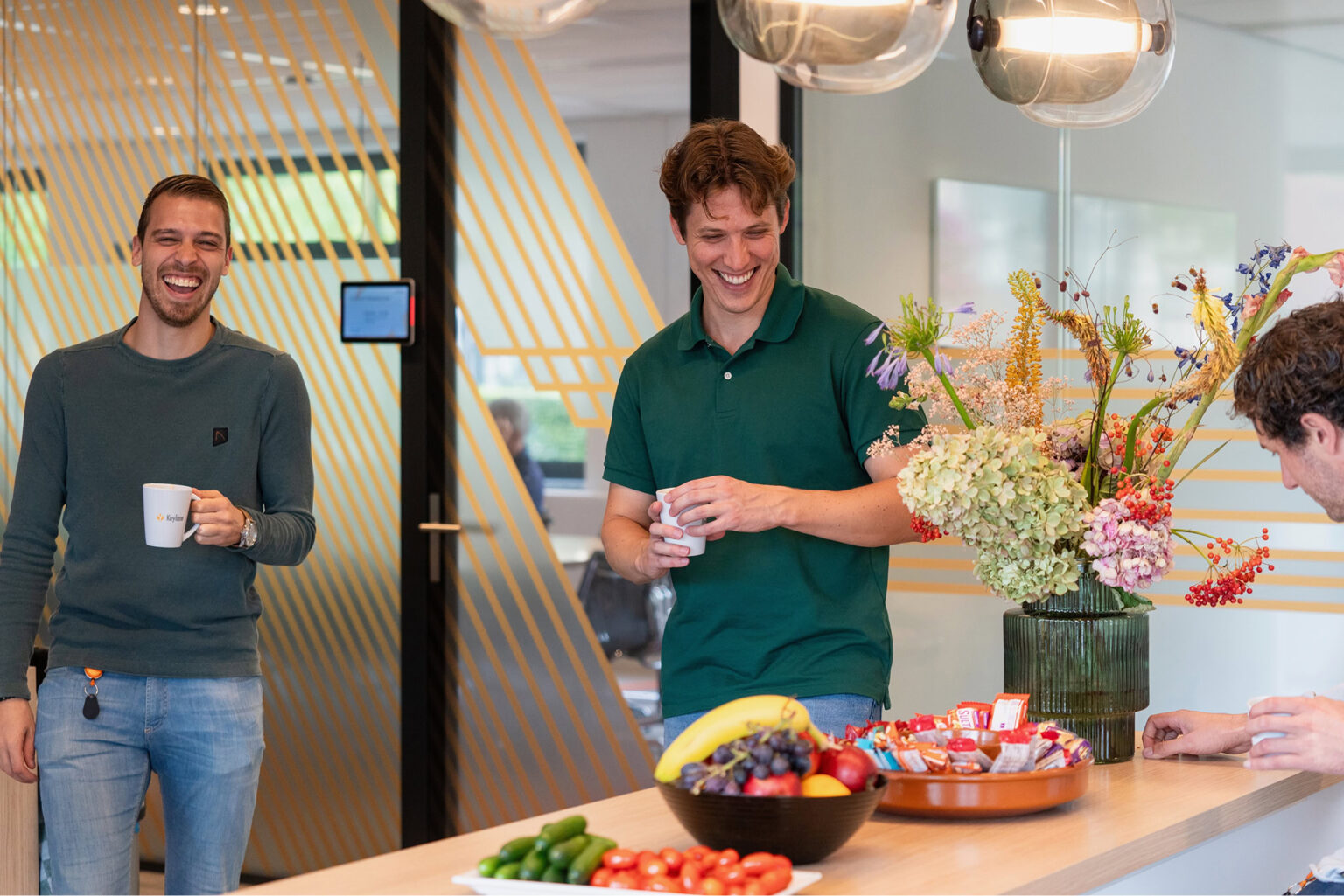 Collaborative team enjoying coffee break at Keylane Careers office with fresh fruit and flowers for a vibrant work environment.
