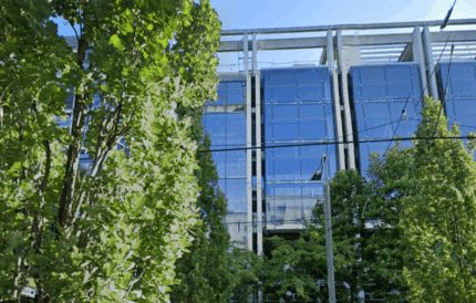 Modern office building with glass facade surrounded by green trees, showcasing innovative work environment, corporate architecture, and sustainable office space at Keylane Careers.