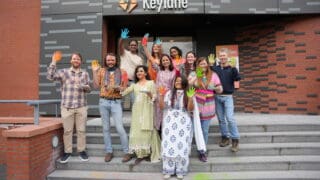 Keylaners stand the entrance to the Keylane Utrecht office, posing for a photo in celebration of Holi, the Hindu festival of colour.
